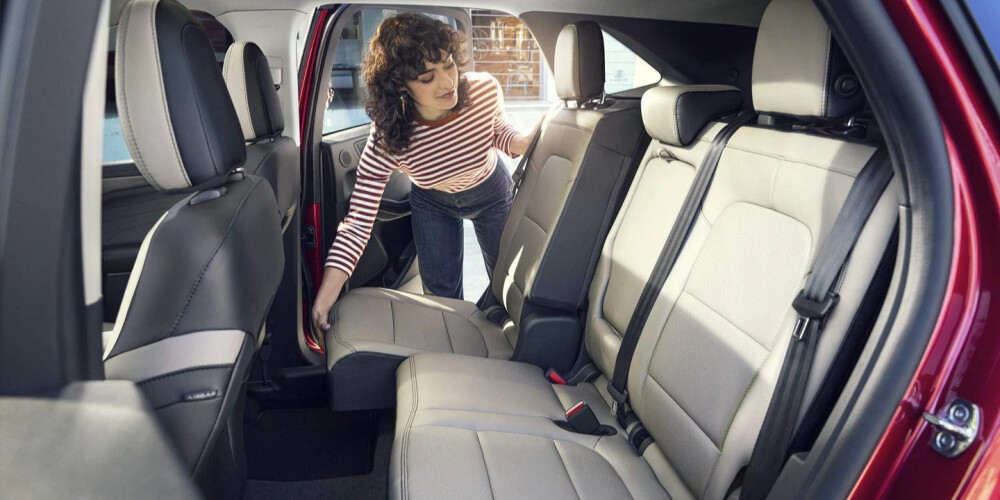 A person with curly hair and a striped shirt adjusts the backseat of a red SUV. The interior is spacious with gray upholstery, conveying practicality.