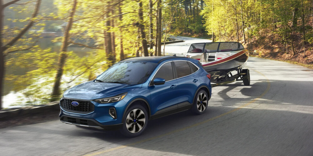 A blue SUV tows a boat on a winding road surrounded by lush green trees, conveying a sense of adventure and tranquility on a sunny day.