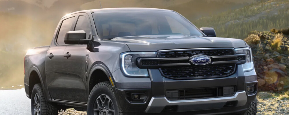 Sleek gray pickup truck with a bold front grille parked by a serene lake, mountain backdrop at sunrise. Rugged and adventurous atmosphere.