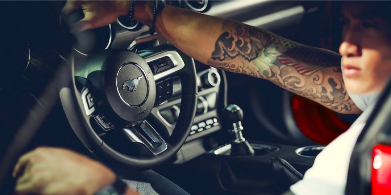 Close up photo of a person holding the steering wheel of a 2024 Ford Mustang